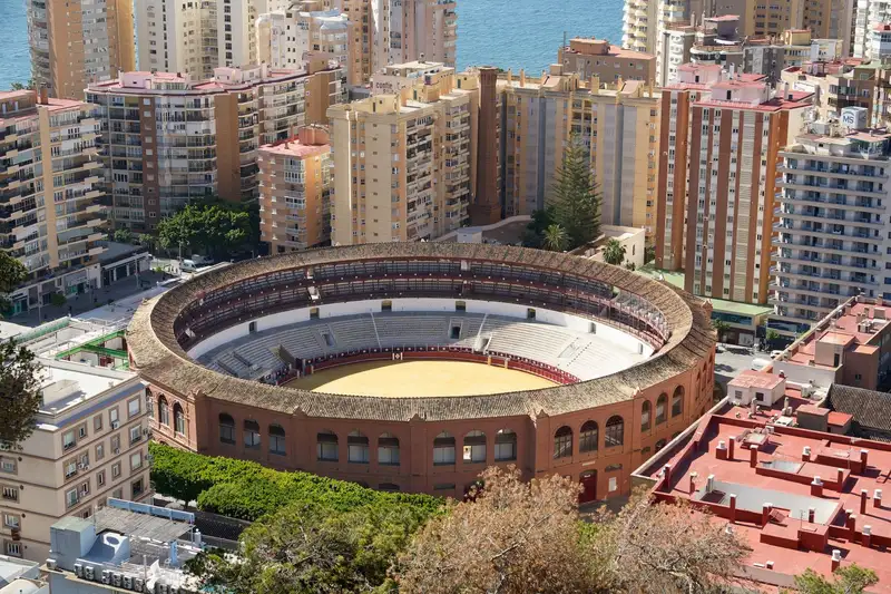 Aerial shot of the iconic bullring in Málaga, surrounded by urban architecture and sea in background.