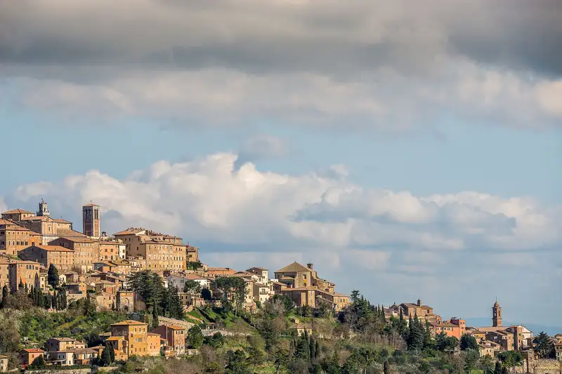 Scenic view of a classic Italian hilltop town under a vast cloudy sky, showcasing historic architecture.