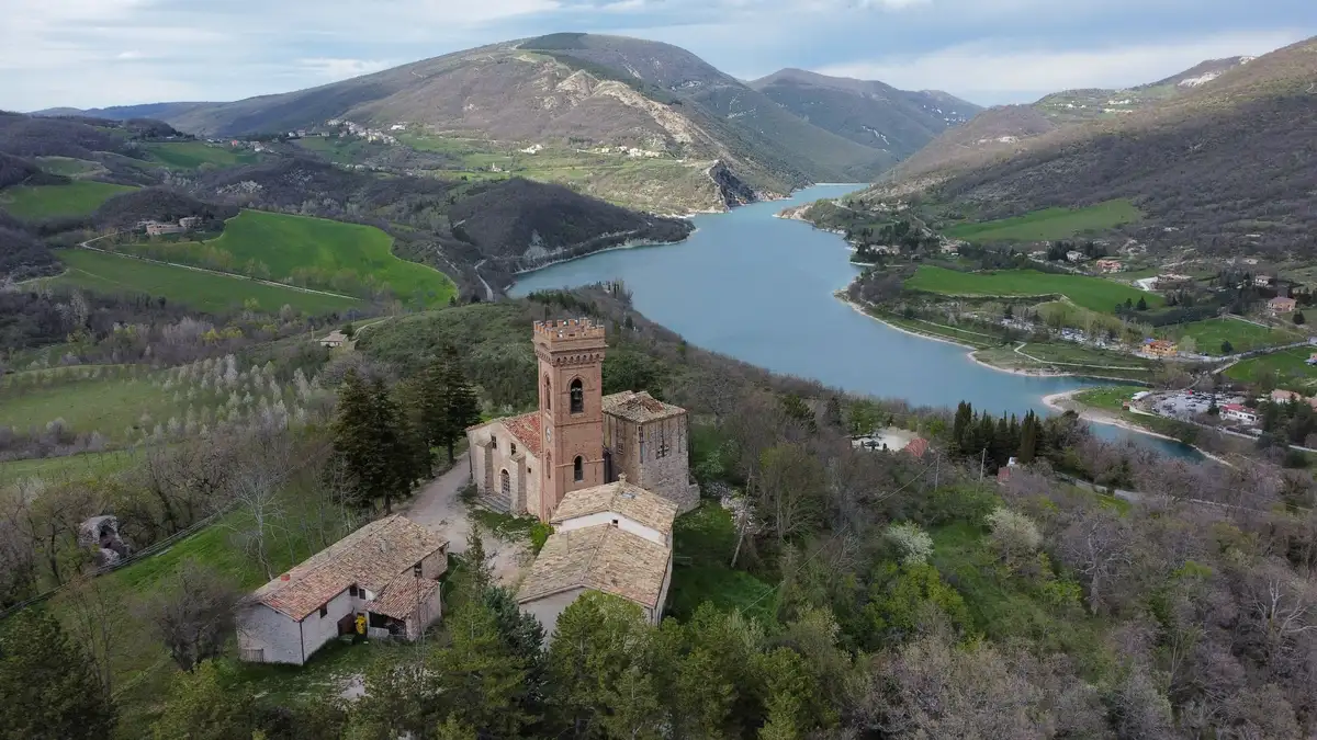 Aerial view of a majestic, weathered historic castle perched on a hill, overlooking a serene blue lake and a lush green valley, perfect for an executive offsite.